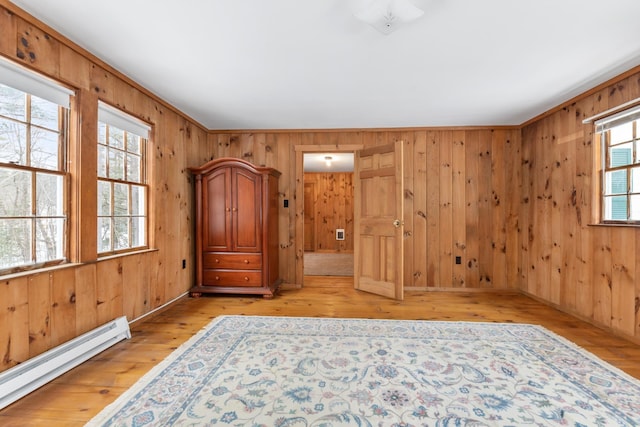 unfurnished bedroom featuring baseboard heating, wooden walls, multiple windows, and light hardwood / wood-style flooring