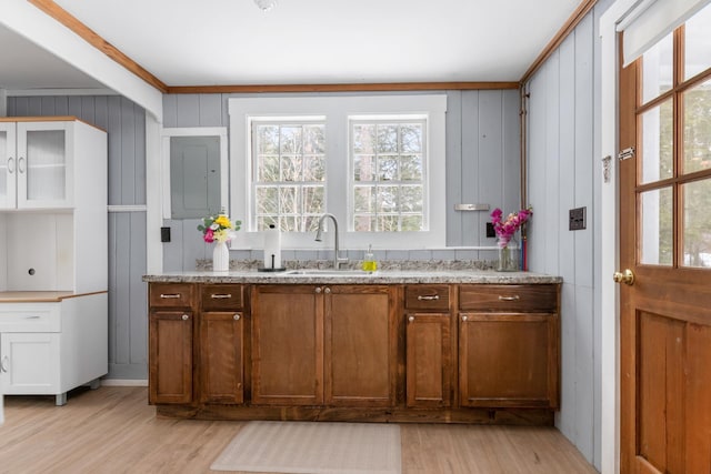 kitchen with light stone counters, sink, wood walls, and light hardwood / wood-style floors