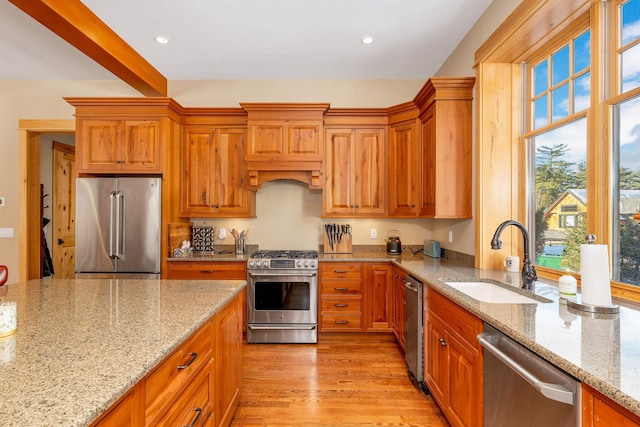 kitchen with beam ceiling, sink, light wood-type flooring, appliances with stainless steel finishes, and light stone counters