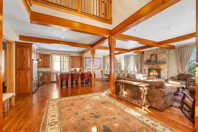 living room with dark hardwood / wood-style floors, beamed ceiling, a stone fireplace, and coffered ceiling