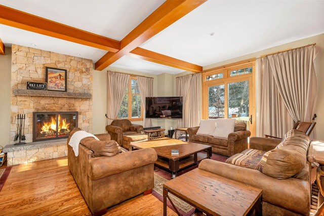 living room featuring coffered ceiling, beam ceiling, light hardwood / wood-style flooring, and a stone fireplace