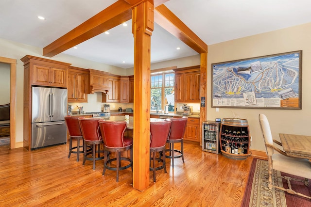 kitchen featuring a center island, light wood-type flooring, a breakfast bar, beam ceiling, and high end fridge