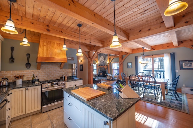 kitchen featuring stainless steel gas stove, hanging light fixtures, beamed ceiling, and a kitchen island