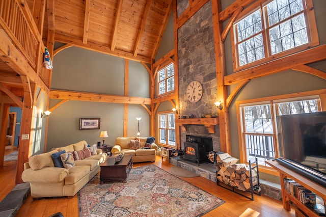 living room with beam ceiling, light hardwood / wood-style flooring, wood ceiling, a wood stove, and high vaulted ceiling