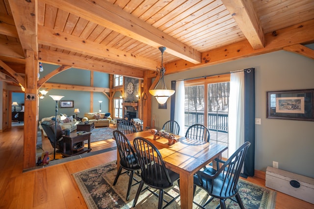 dining space featuring beam ceiling, light wood-type flooring, a fireplace, and wood ceiling