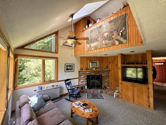 carpeted living room featuring a brick fireplace, a textured ceiling, lofted ceiling with skylight, and ceiling fan