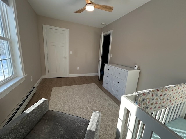 bedroom with ceiling fan, a baseboard heating unit, dark hardwood / wood-style flooring, and a crib