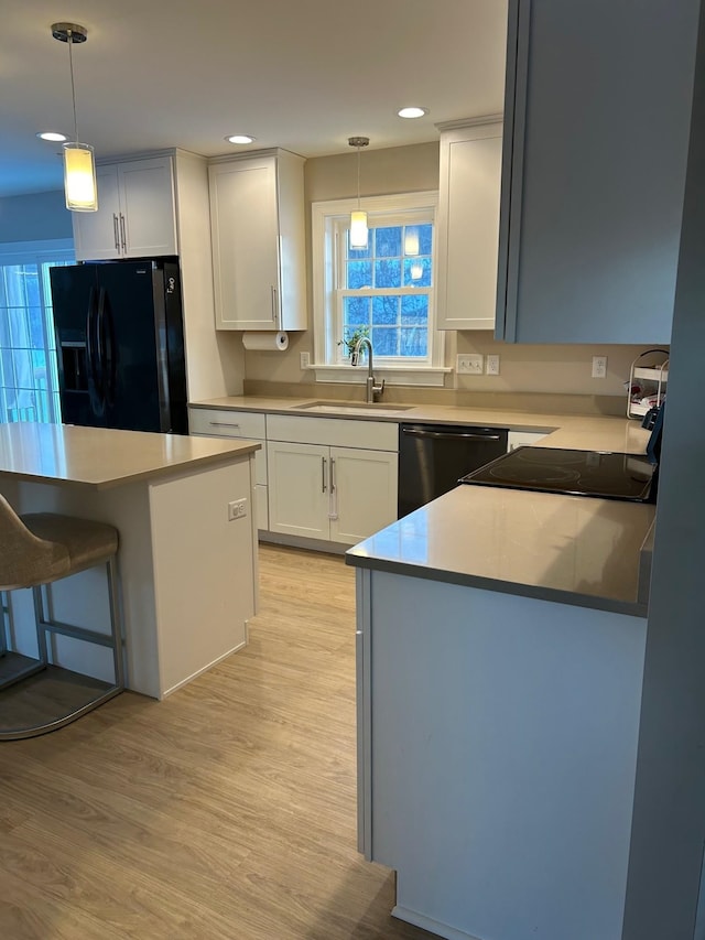 kitchen featuring black appliances, decorative light fixtures, white cabinetry, sink, and light hardwood / wood-style flooring