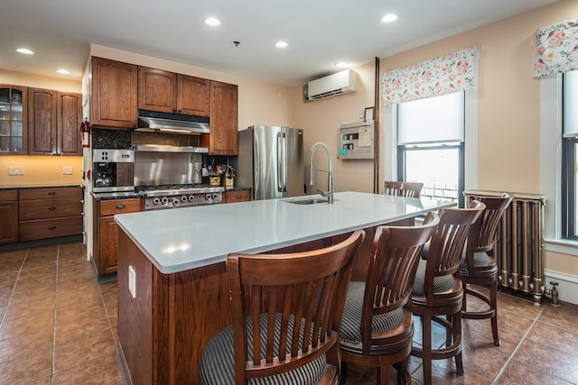 kitchen with sink, stainless steel fridge, an island with sink, and a wall unit AC