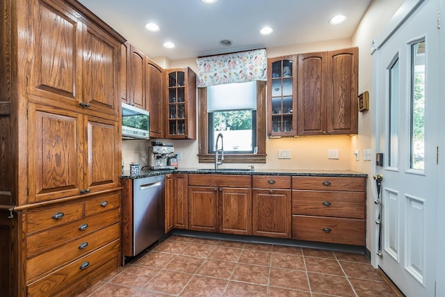 kitchen with appliances with stainless steel finishes, sink, dark tile patterned flooring, and dark stone counters