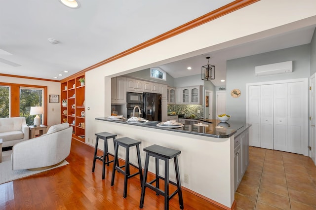 kitchen featuring a kitchen bar, a wall unit AC, hanging light fixtures, black appliances, and sink