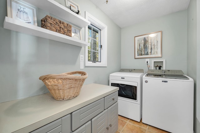 laundry area with light tile patterned floors, cabinets, a textured ceiling, and washer and clothes dryer