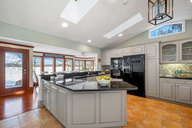 kitchen featuring vaulted ceiling with skylight, black appliances, a kitchen island, tasteful backsplash, and light tile patterned floors