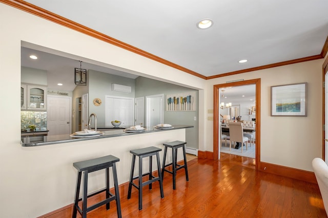 kitchen featuring a kitchen bar, hardwood / wood-style floors, kitchen peninsula, hanging light fixtures, and crown molding