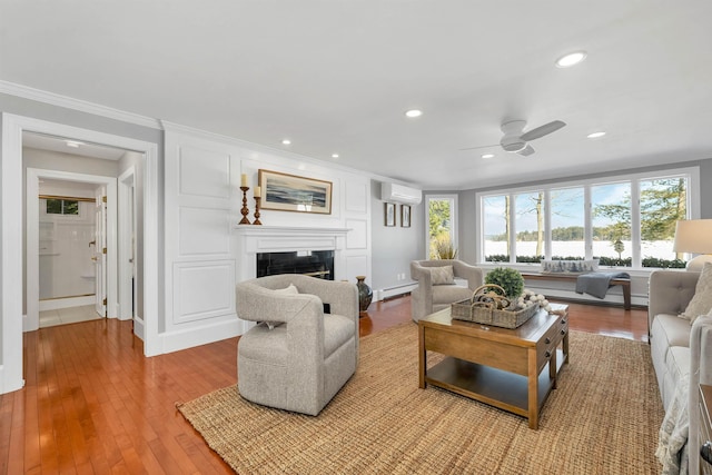 living room with ceiling fan, a baseboard heating unit, light hardwood / wood-style floors, a wall mounted air conditioner, and ornamental molding