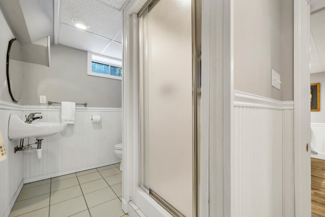 bathroom with toilet, walk in shower, a drop ceiling, tile patterned flooring, and wood walls