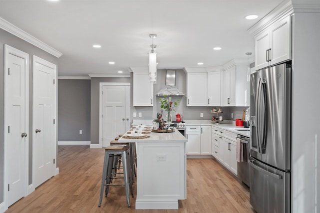 kitchen featuring white cabinetry, appliances with stainless steel finishes, hanging light fixtures, a kitchen island, and wall chimney exhaust hood