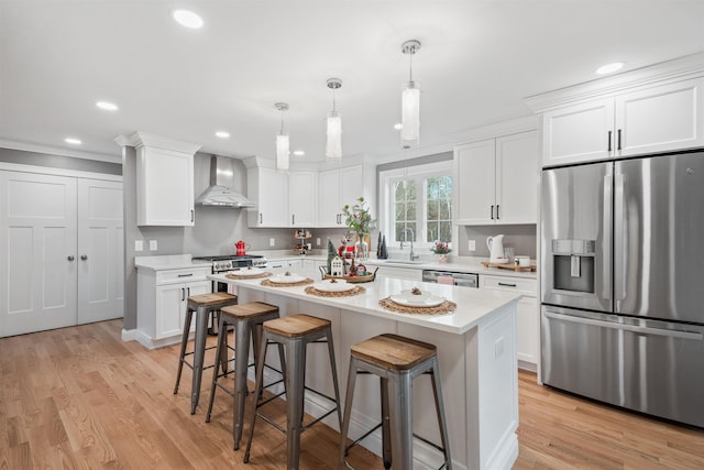 kitchen with white cabinetry, wall chimney range hood, appliances with stainless steel finishes, and a kitchen island