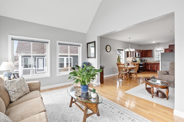 living room with vaulted ceiling, an inviting chandelier, and light hardwood / wood-style floors