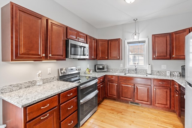 kitchen featuring light stone countertops, sink, hanging light fixtures, and stainless steel appliances