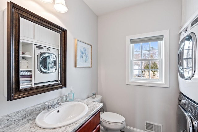 bathroom featuring stacked washer / drying machine, vanity, and toilet