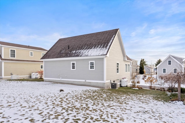 snow covered rear of property featuring central AC