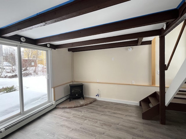 unfurnished living room with baseboard heating, a wood stove, hardwood / wood-style floors, and vaulted ceiling with beams