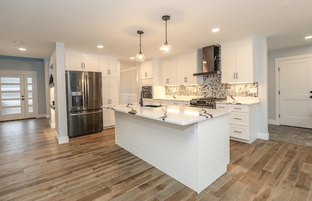 kitchen with white cabinetry, wall chimney range hood, stainless steel appliances, sink, and a kitchen island with sink