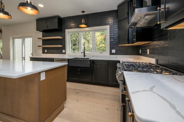 kitchen featuring decorative light fixtures, stainless steel gas range, light stone counters, and light hardwood / wood-style flooring