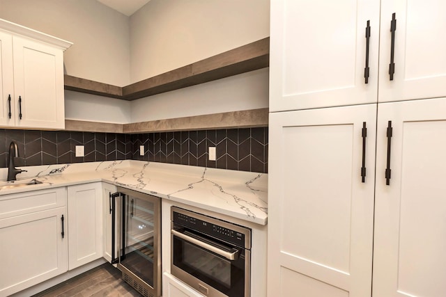 kitchen featuring white cabinetry, decorative backsplash, wine cooler, light stone counters, and sink