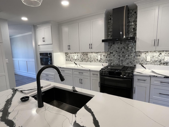 kitchen with black appliances, white cabinets, and wall chimney range hood