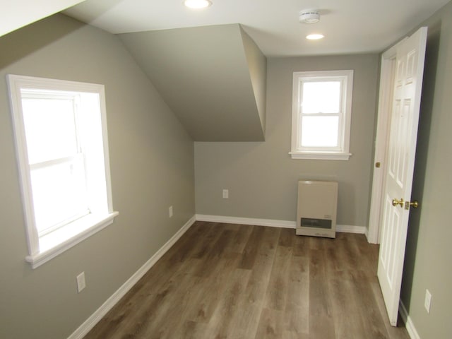 additional living space with heating unit, dark hardwood / wood-style flooring, and vaulted ceiling