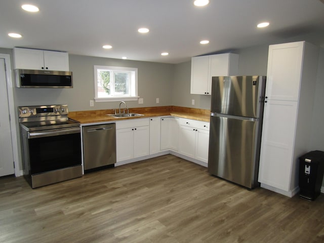 kitchen featuring hardwood / wood-style flooring, butcher block countertops, appliances with stainless steel finishes, white cabinets, and sink