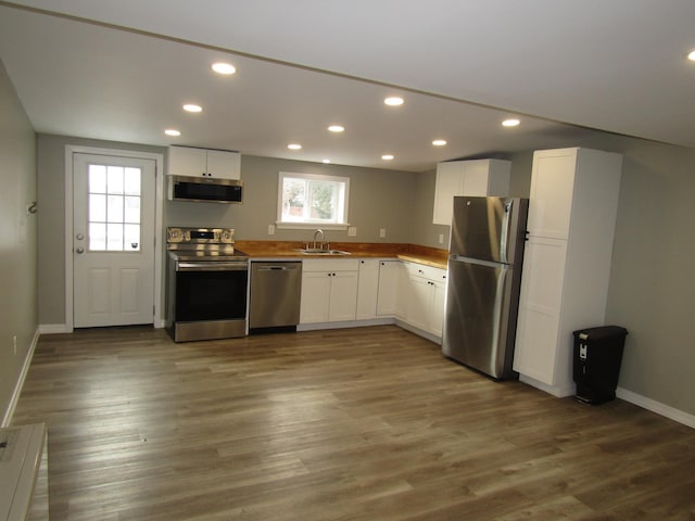 kitchen featuring wood-type flooring, appliances with stainless steel finishes, sink, and white cabinetry