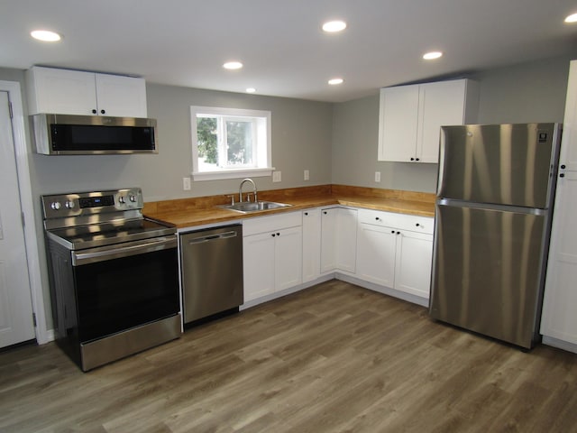 kitchen with dark hardwood / wood-style floors, butcher block countertops, sink, stainless steel appliances, and white cabinets