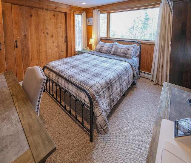 carpeted bedroom with a baseboard heating unit and wooden walls