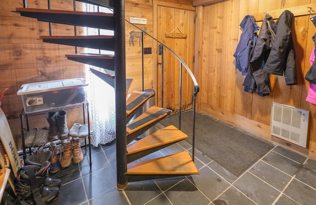 stairway featuring heating unit, tile patterned flooring, and wood walls