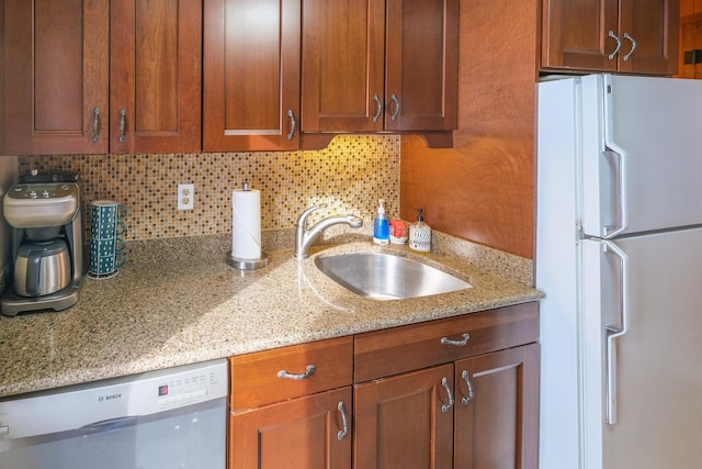 kitchen with backsplash, light stone countertops, white refrigerator, stainless steel dishwasher, and sink