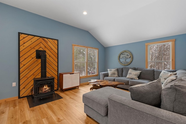 living room featuring a wood stove, light wood-style floors, baseboards, and vaulted ceiling