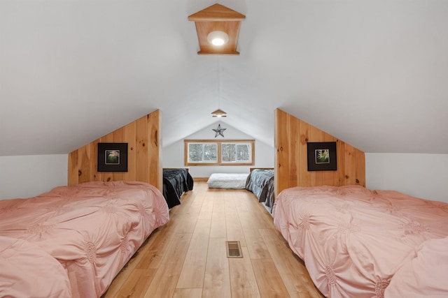 bedroom featuring lofted ceiling, light wood finished floors, visible vents, and wooden walls