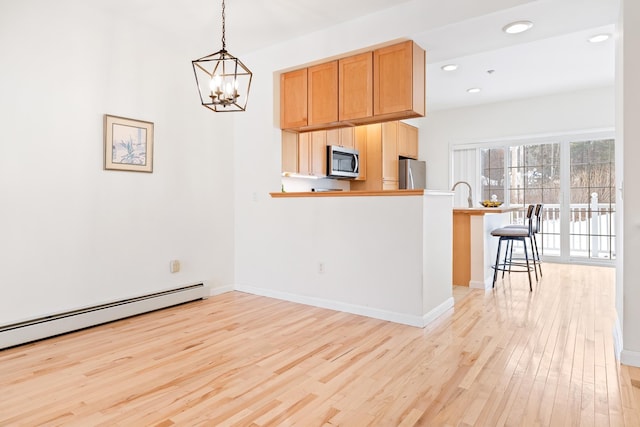 kitchen featuring light hardwood / wood-style floors, a kitchen bar, kitchen peninsula, stainless steel appliances, and hanging light fixtures