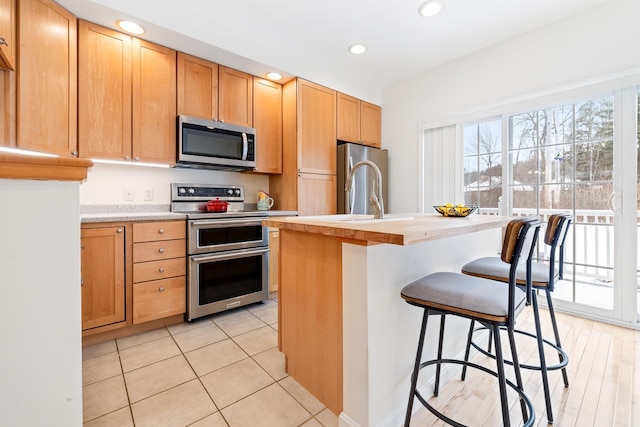 kitchen featuring a kitchen bar, stainless steel appliances, an island with sink, sink, and light tile patterned floors