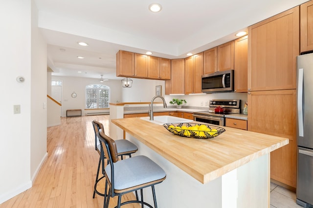 kitchen with a center island with sink, a breakfast bar area, stainless steel appliances, light hardwood / wood-style flooring, and sink