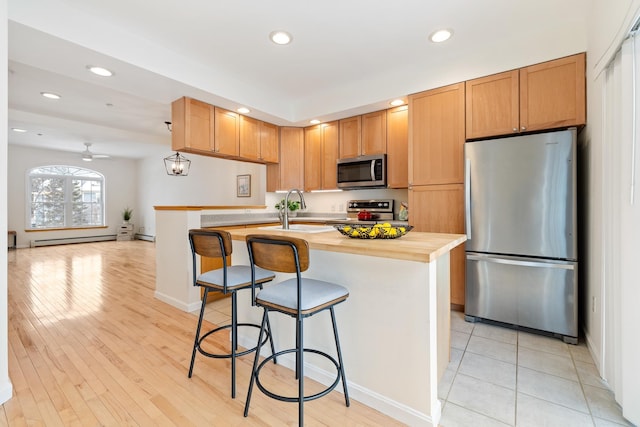 kitchen with a baseboard heating unit, stainless steel appliances, sink, a kitchen island with sink, and ceiling fan