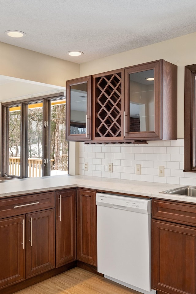 kitchen with decorative backsplash, a textured ceiling, dishwasher, and light wood-type flooring