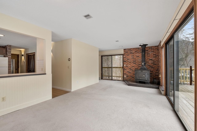 unfurnished living room featuring carpet floors, a wood stove, and a baseboard heating unit