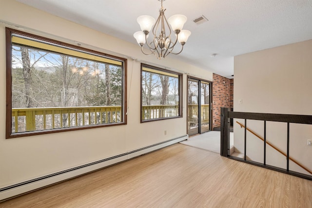 unfurnished room featuring light wood-type flooring, a healthy amount of sunlight, a baseboard heating unit, and a chandelier