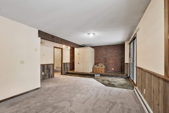 empty room featuring a baseboard heating unit, wooden walls, a textured ceiling, and dark colored carpet