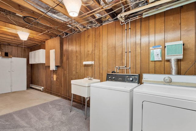 clothes washing area with wooden walls, washer and dryer, baseboard heating, carpet flooring, and sink