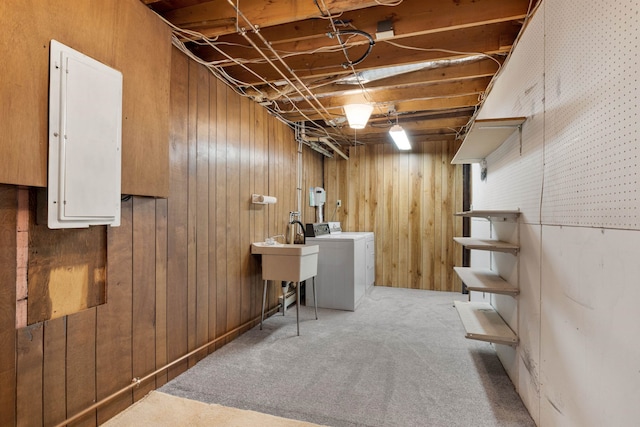 basement with wood walls, washer and dryer, light colored carpet, electric panel, and sink